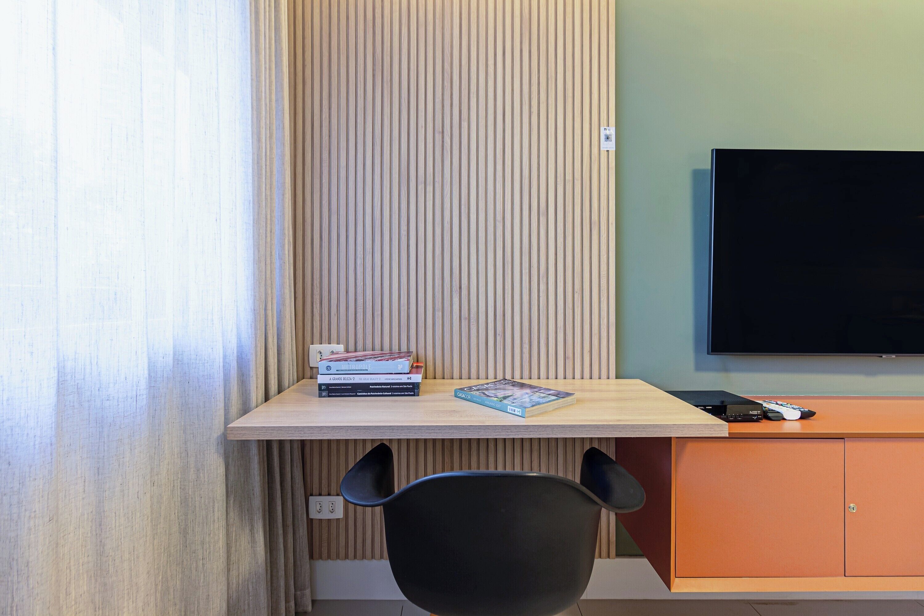 Una habitación con un escritorio de madera, una silla negra, un televisor y una pila de libros.