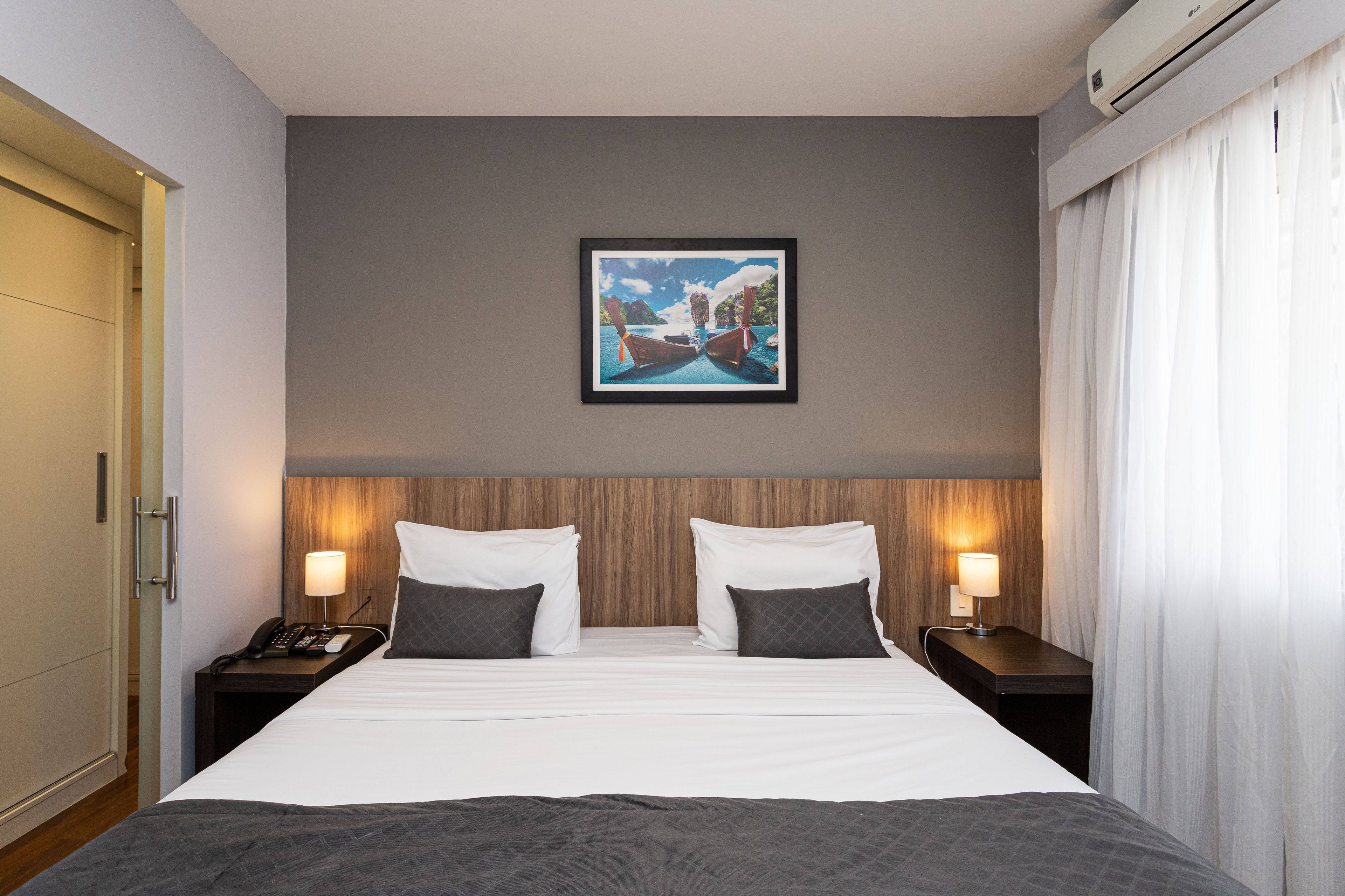 Una camera d'albergo con un letto grande, due comodini con lampade, un quadro appeso alla parete e una testiera in legno.