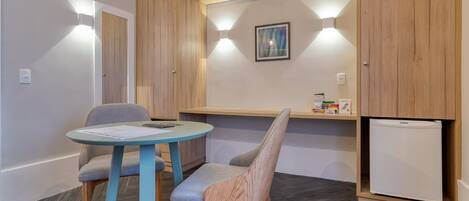 Una habitación compacta con una mesa redonda y dos sillas, un refrigerador pequeño y una estantería con objetos.