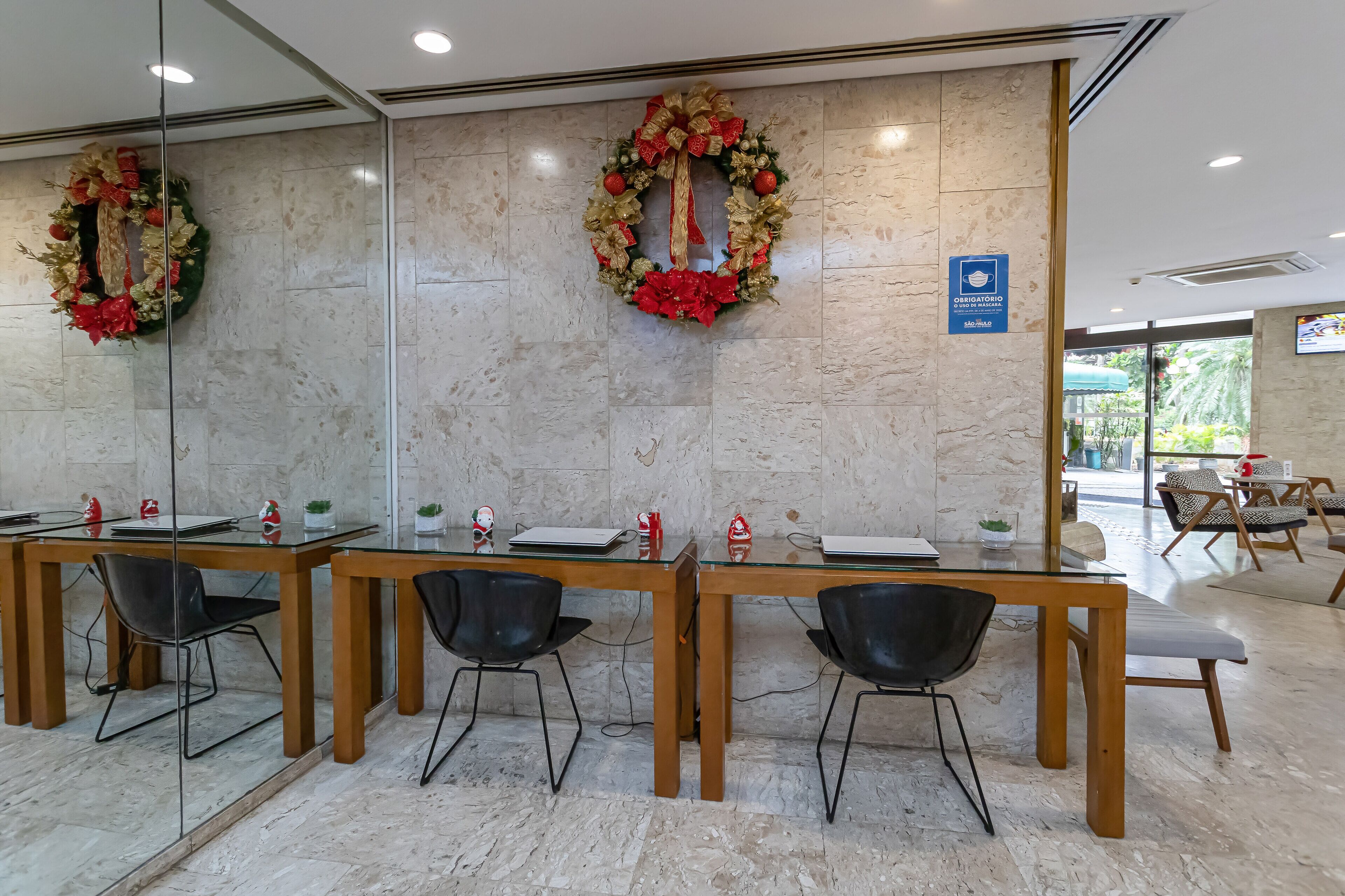 A reception area with a marble wall, two Christmas wreaths, a blue sign, and a glass partition.