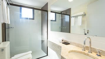 Un baño moderno con ducha envuelta en vidrio, inodoro, lavabo con encimera de mármol y un espejo grande.