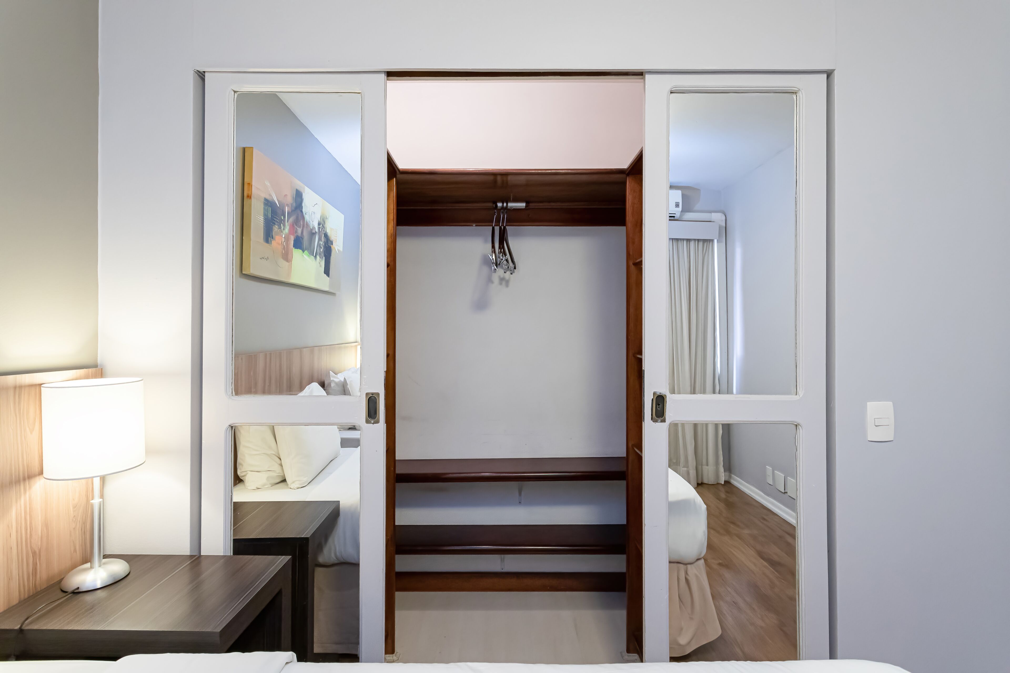 Habitación de hotel con literas, una mesita de noche con lámpara, un cuadro en la pared y una puerta que da a otra habitación.