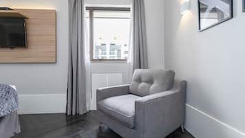 A modern room with a grey upholstered armchair, a wooden panel wall, a flat-screen TV, and a window with curtains.
