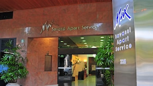 La entrada a Max Savassi Apart Service, con un diseño moderno que incluye un mostrador de recepción, plantas en macetas y una vista despejada del interior.