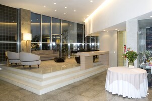 Un vestíbulo moderno con zona de estar, mostrador de recepción y escalera que sube a un nivel superior.