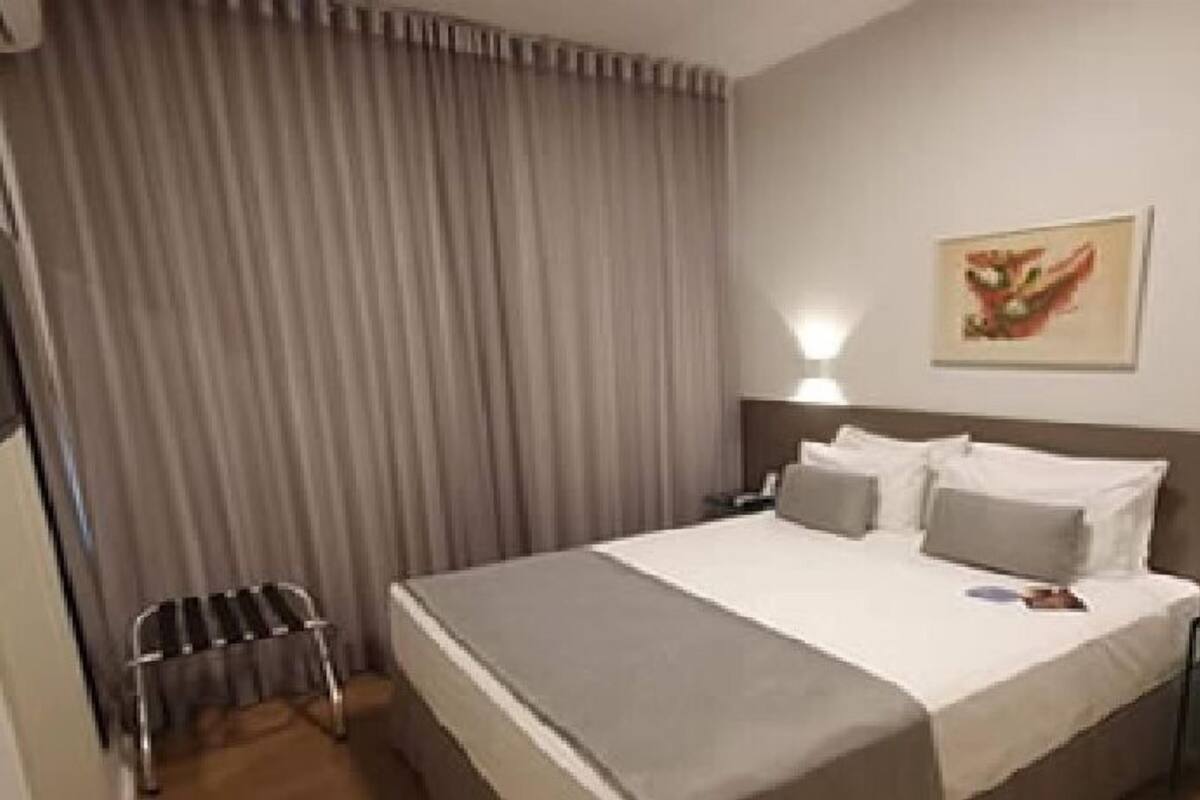 Une chambre d’hôtel avec un lit, une table de chevet, une lampe, une chaise et un tableau au mur.