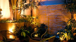 Un patio con sillas de mimbre, plantas en macetas y un muro de ladrillo.