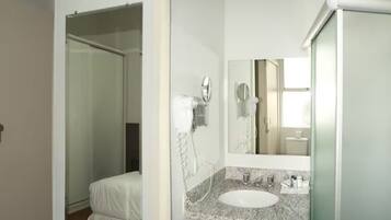 A hotel bathroom with a white sink, a mirror, a hairdryer, and a towel hanging on the wall.