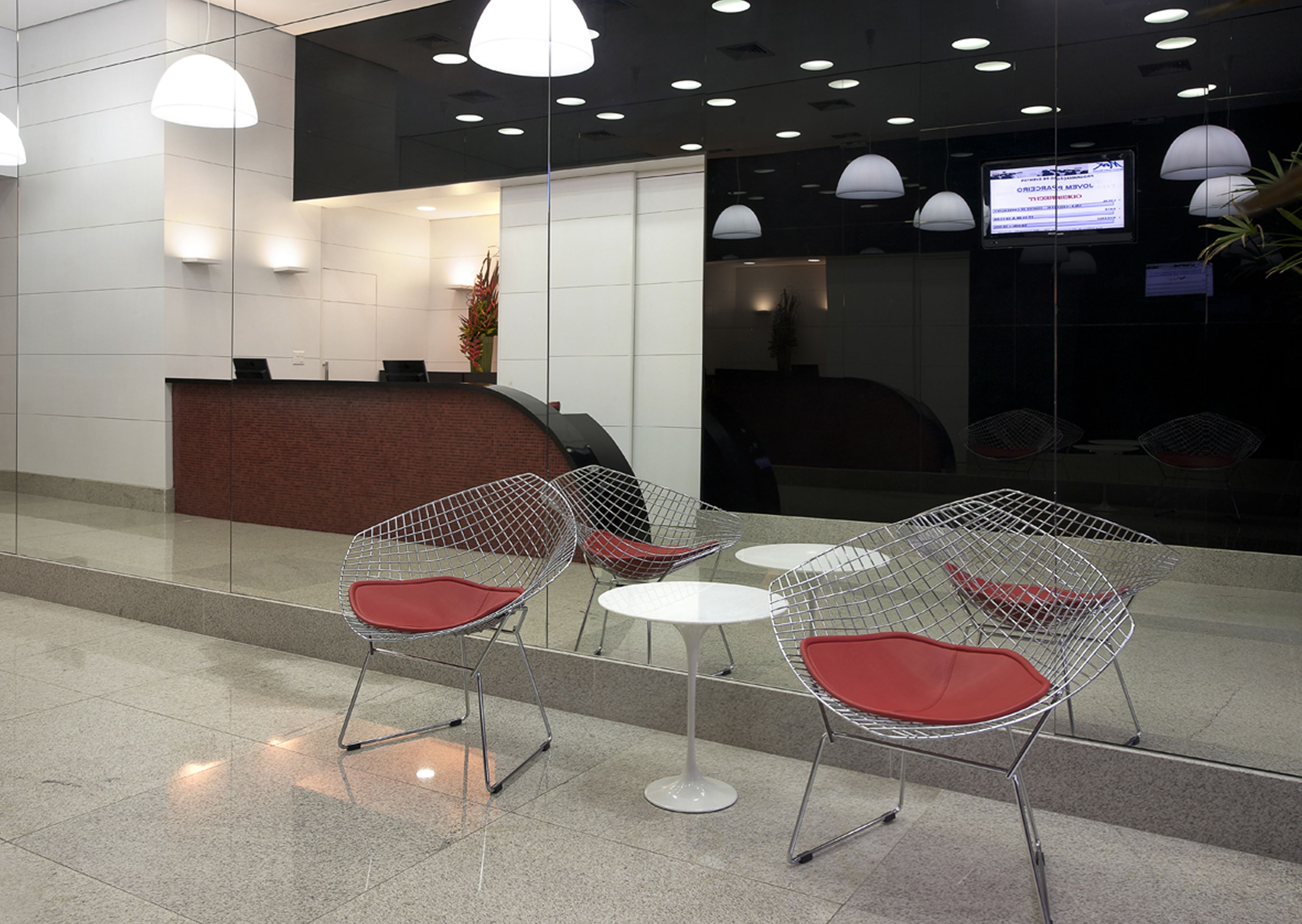 A reception area with a reception desk, a seating area with metal chairs and tables, and a large screen displaying information.