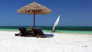 Une plage avec deux chaises longues et un parasol en paille.