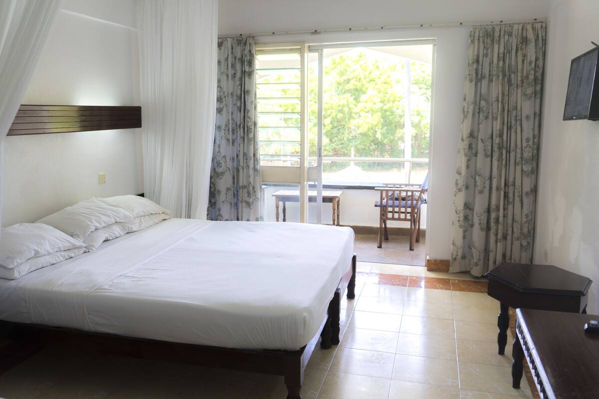 Un dormitorio con una cama, una mesita de noche de madera, una pequeña mesa y una silla.