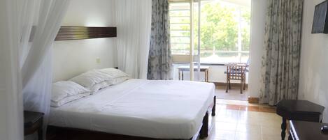 A bedroom with a bed, a wooden nightstand, a small table, and a chair.