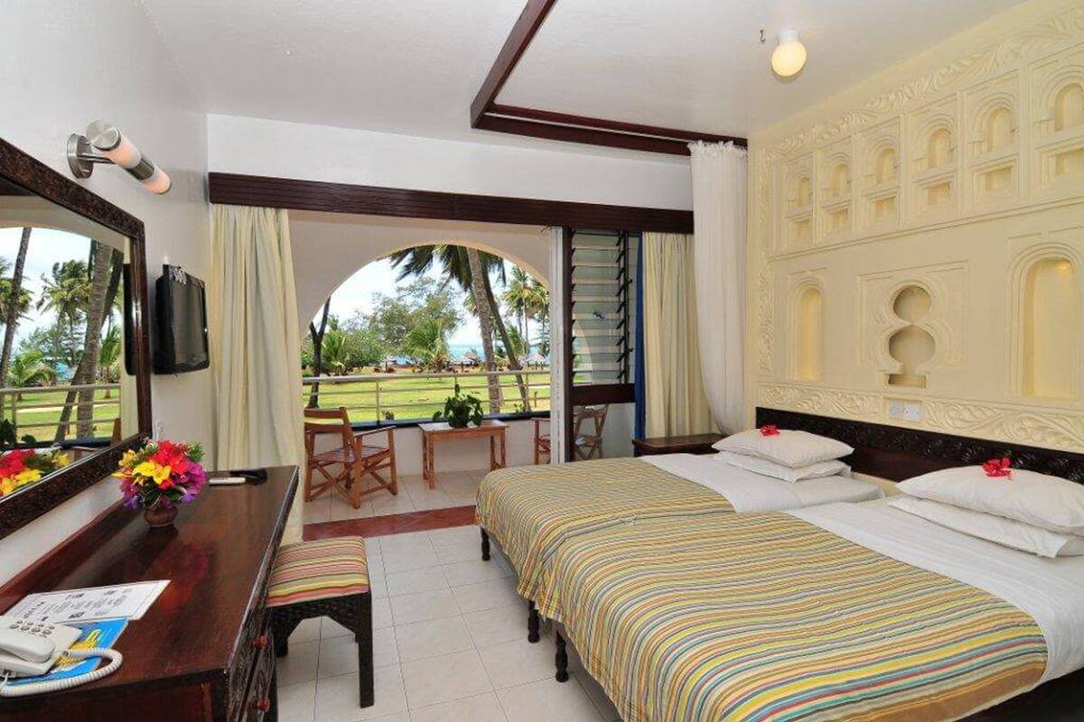 Habitación de hotel con una cama grande, un escritorio con teléfono y vistas a un campo de golf a través de una puerta abierta.