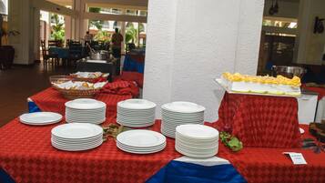 A buffet setup with multiple tables covered in red and blue tablecloths, featuring stacks of white plates and a tray of yellow food.