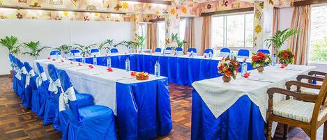 Un salón de conferencias con varias mesas, manteles azules y sillas.
