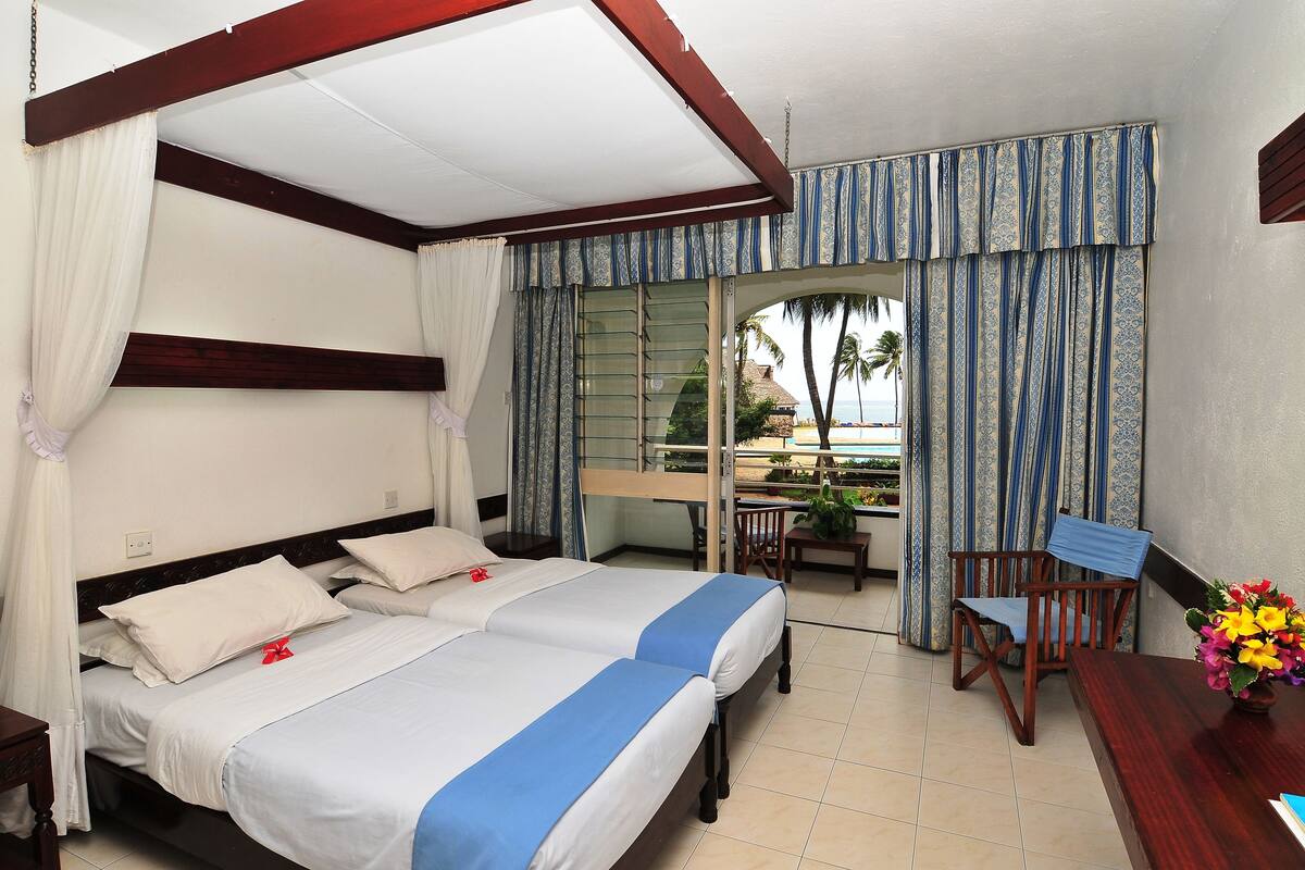 Habitación de hotel con dos camas, un escritorio y vista al océano.