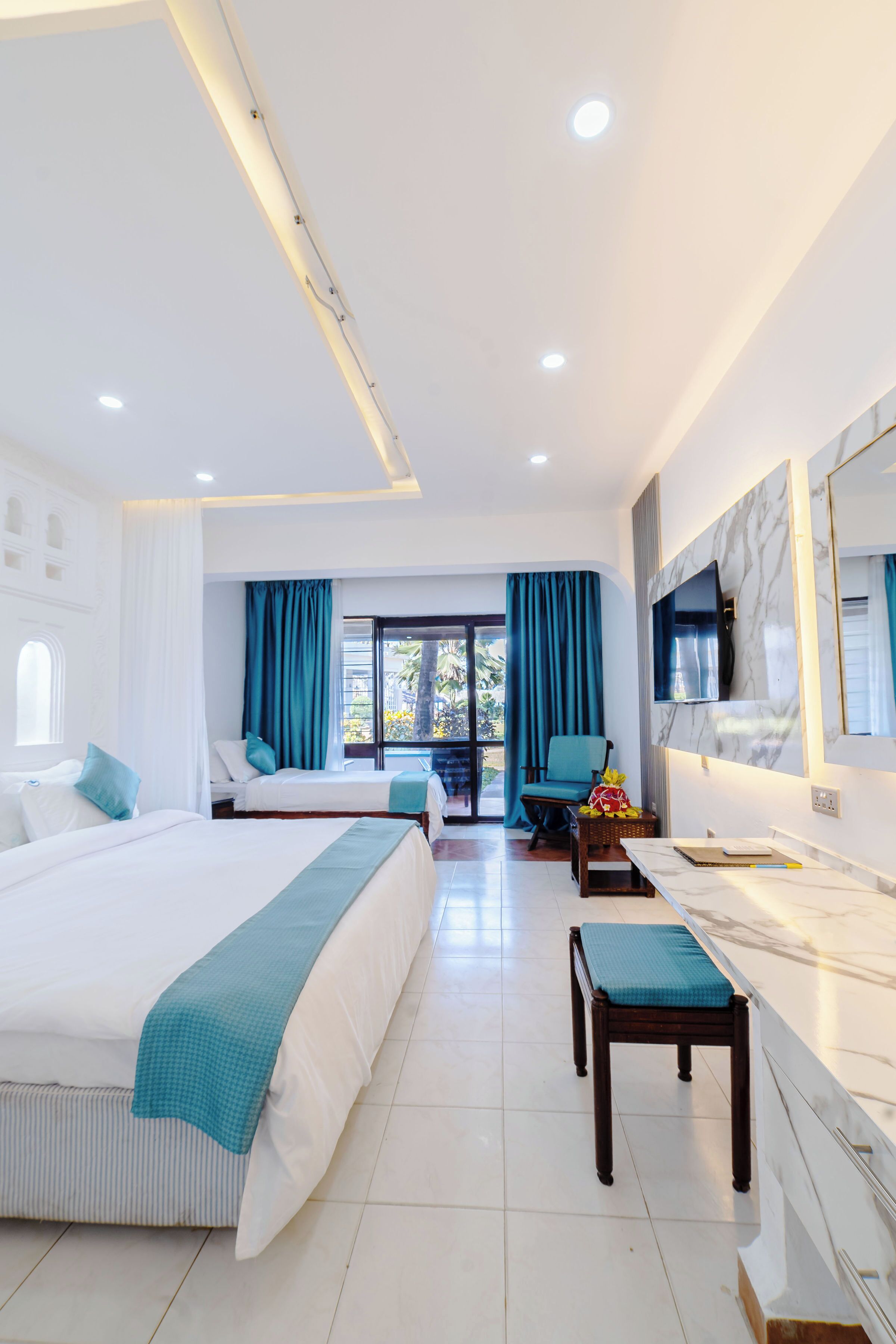 A hotel room with two beds, a desk, a chair, a TV, and a large window with curtains.