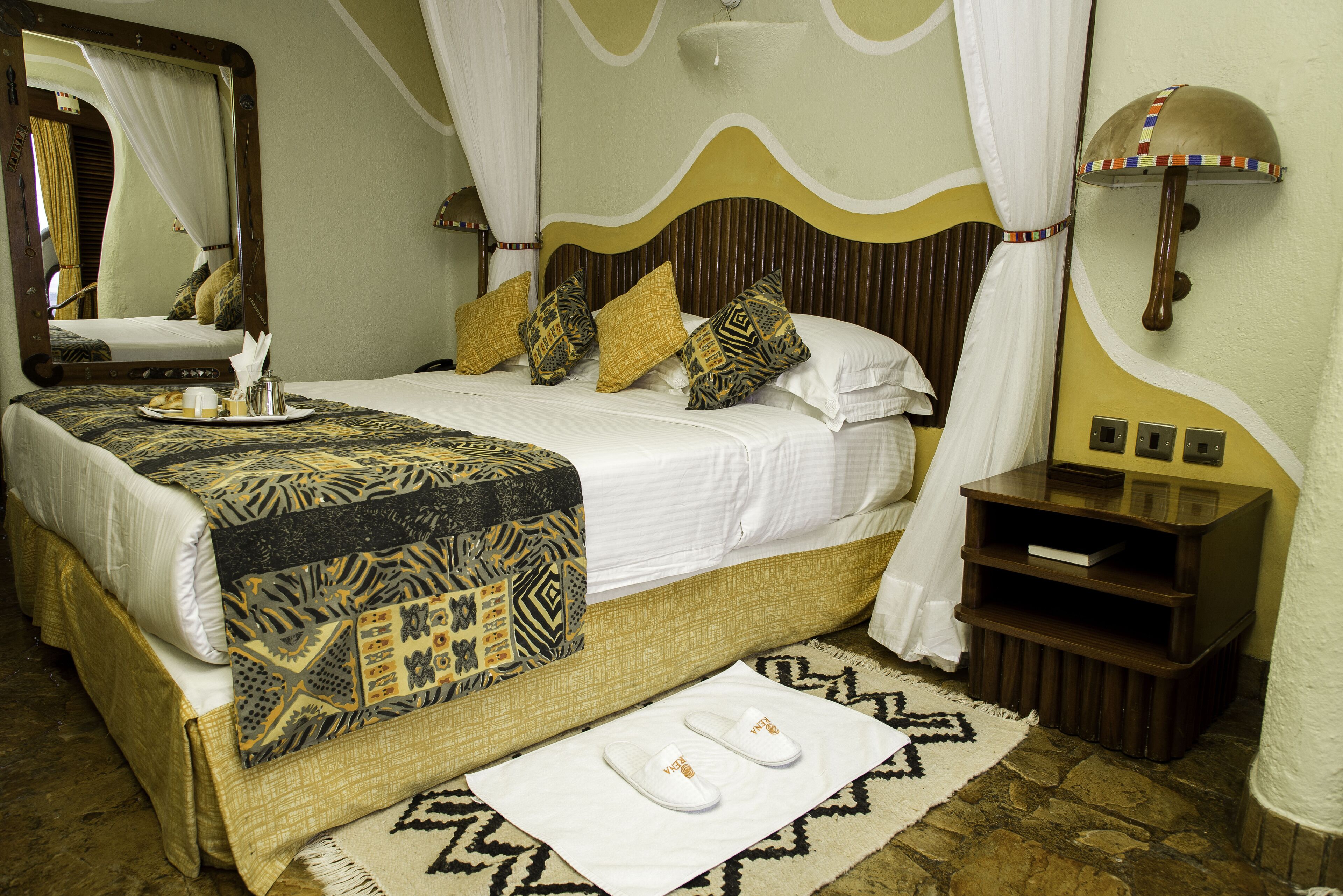 A neatly made bed with a patterned bedspread, a bedside table with a lamp, and a mirror on the wall.