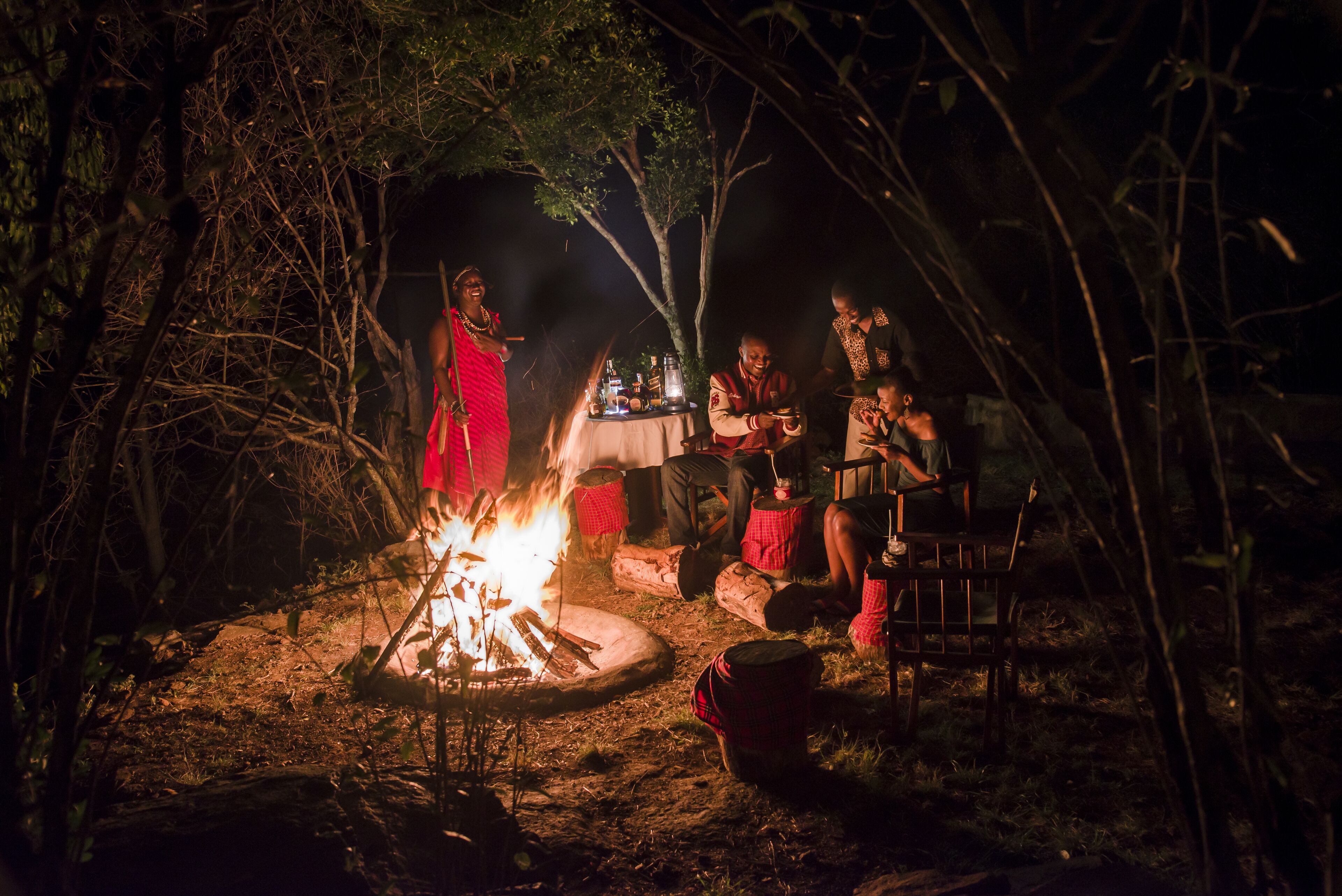Un grupo de personas reunidas alrededor de una fogata en un área boscosa durante la noche.