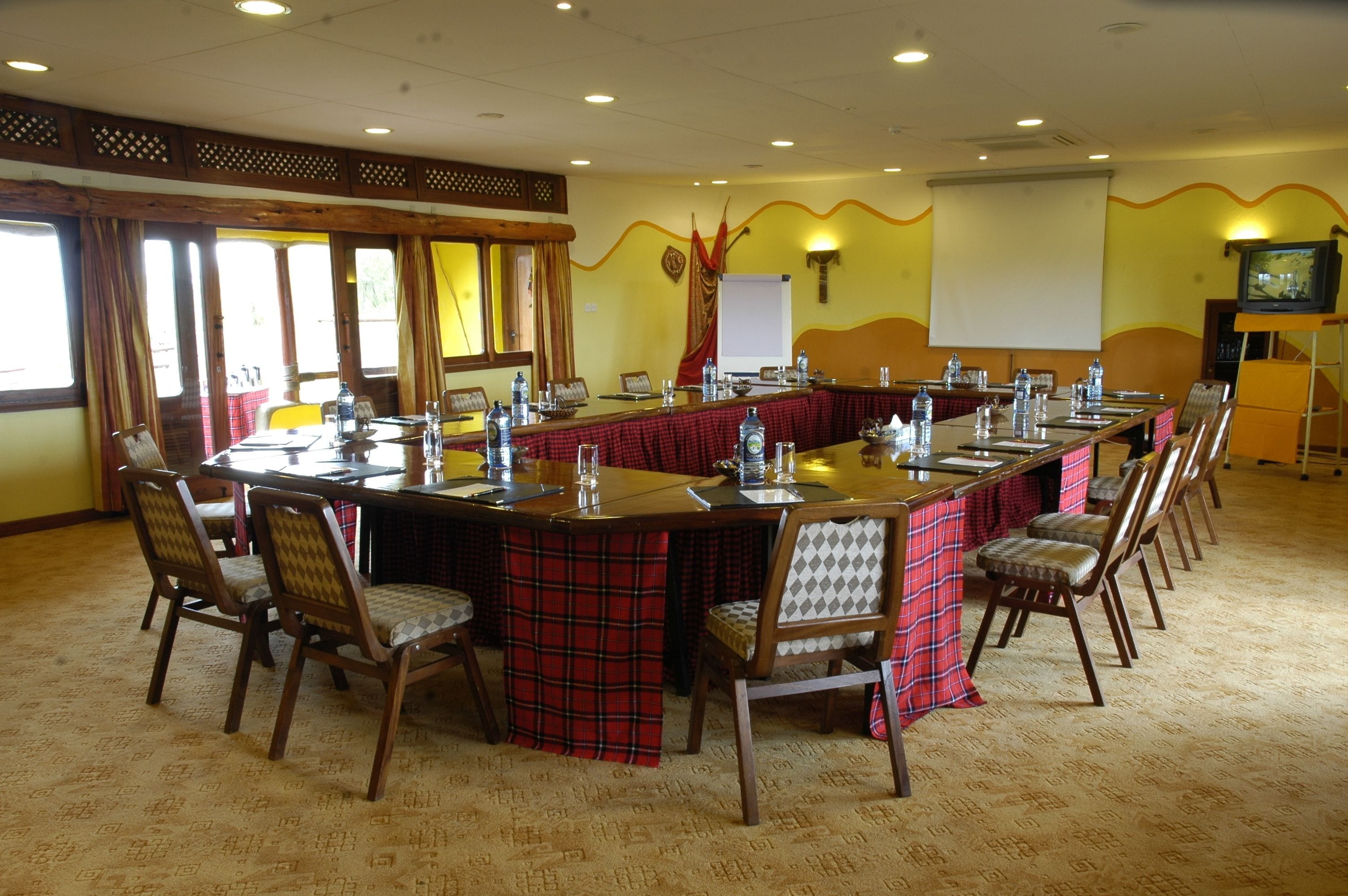 A conference room with a long table, chairs, a projector screen, and a television.