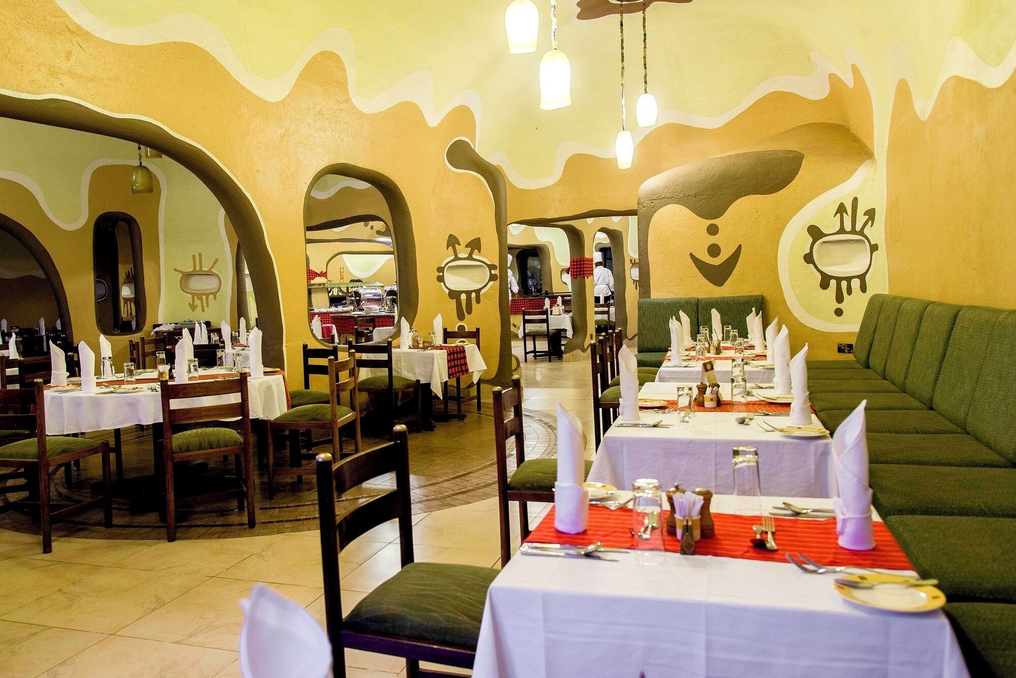 A restaurant with tables set for dining, a chef in the background, and a unique wavy wall design.