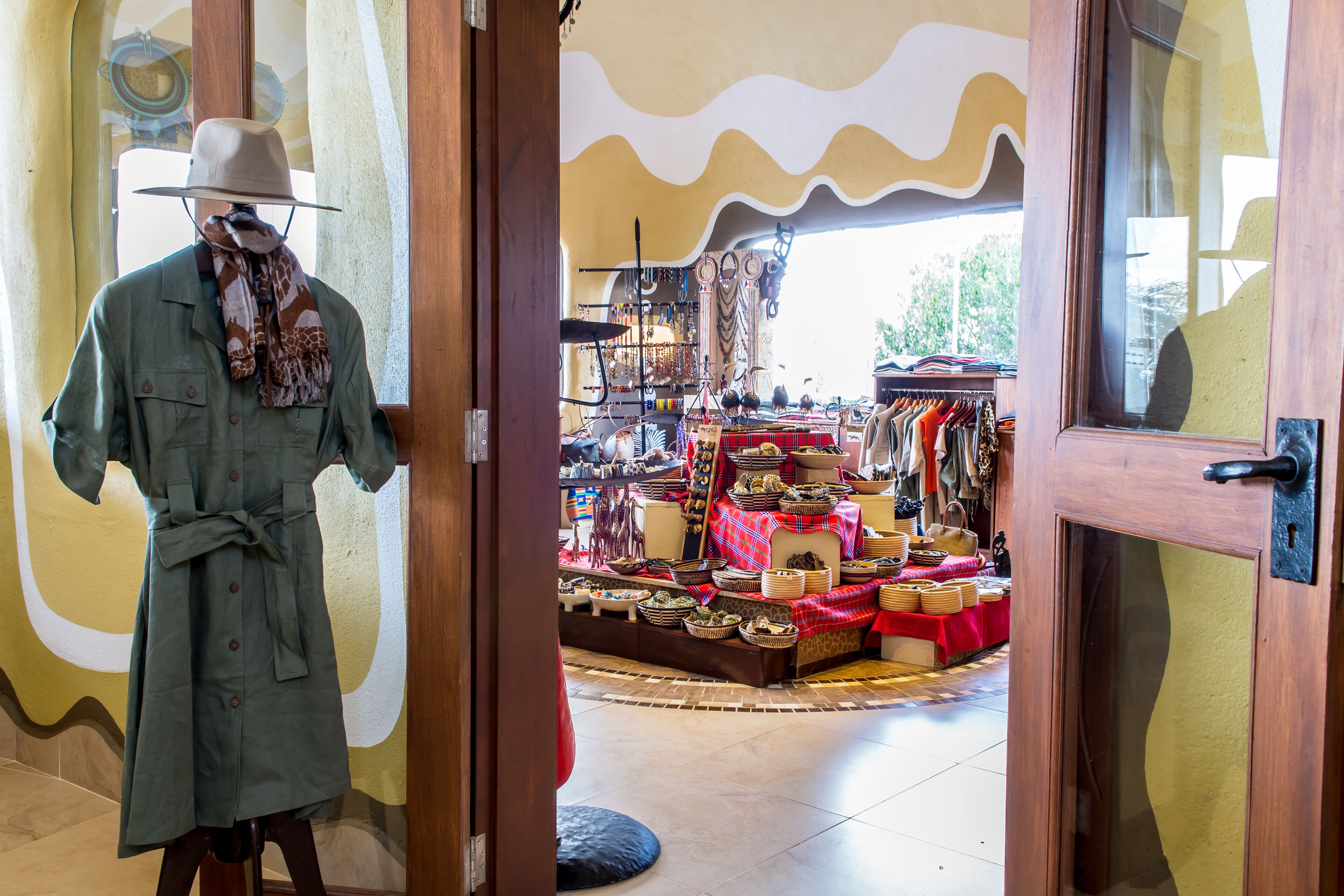 Un maniquí con abrigo y sombrero verdes, exhibición de cestas y textiles, y una zona cubierta con mantel rojo.