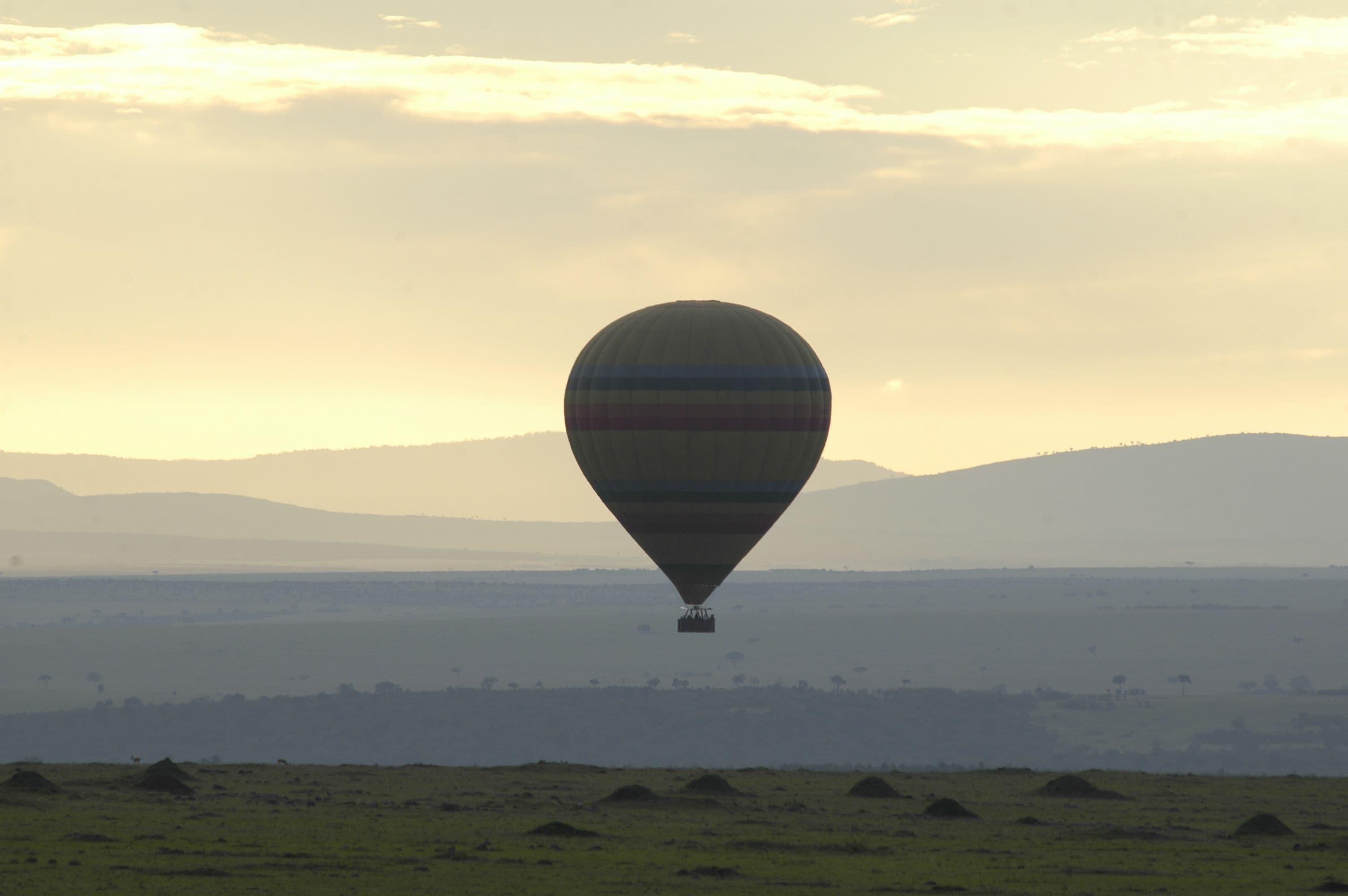 A hot air balloon over a flat landscape with distant hills.