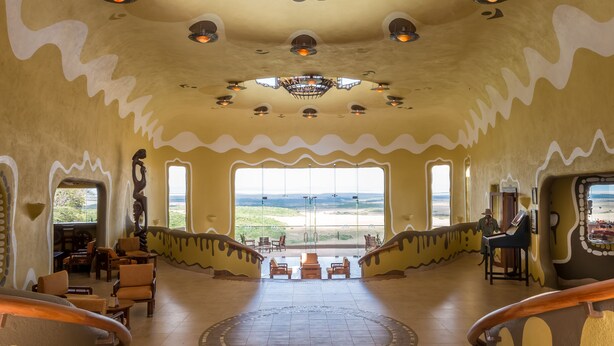 A spacious lobby with a central seating area, large windows offering a view of the landscape, and a unique ceiling design.
