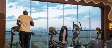 Un gimnasio con un amplio ventanal que ofrece vistas a un paisaje pintoresco, con cintas de correr y máquinas elípticas.