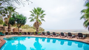 A pool with lounge chairs and palm trees, overlooking a beach.