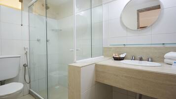 A modern bathroom with a glass-enclosed shower, a white toilet, and a sink with a mirror above it.
