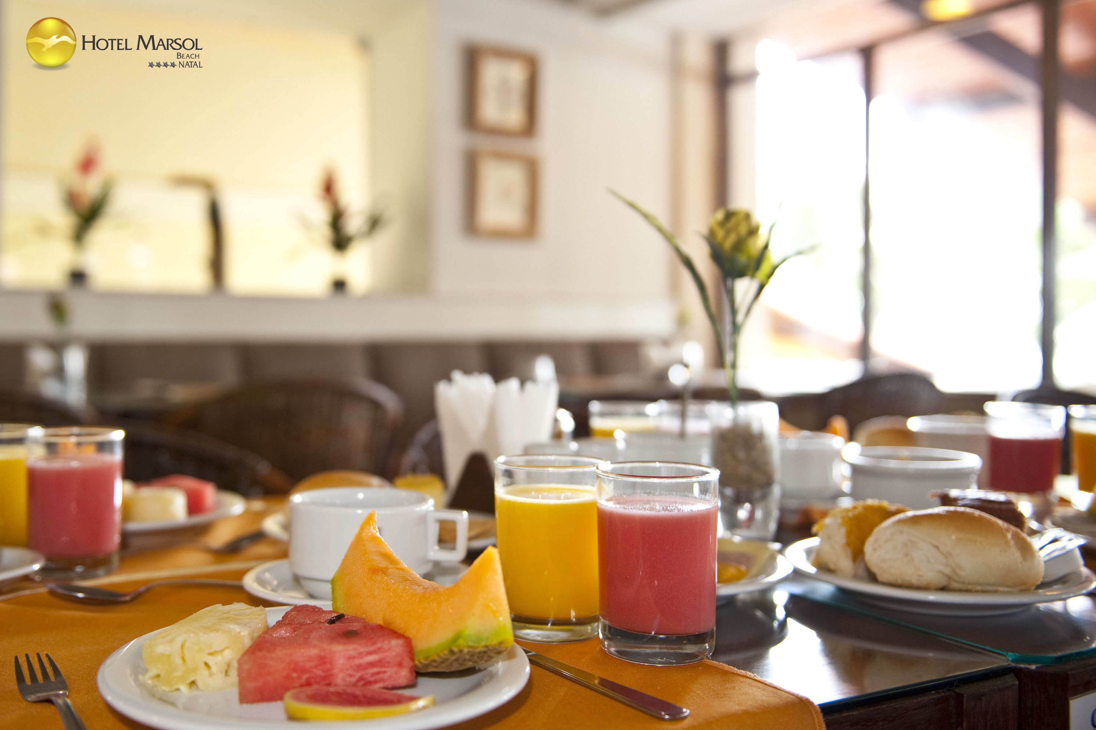 A breakfast table with various fruits, juices, and pastries, indicating a hotel breakfast setting.