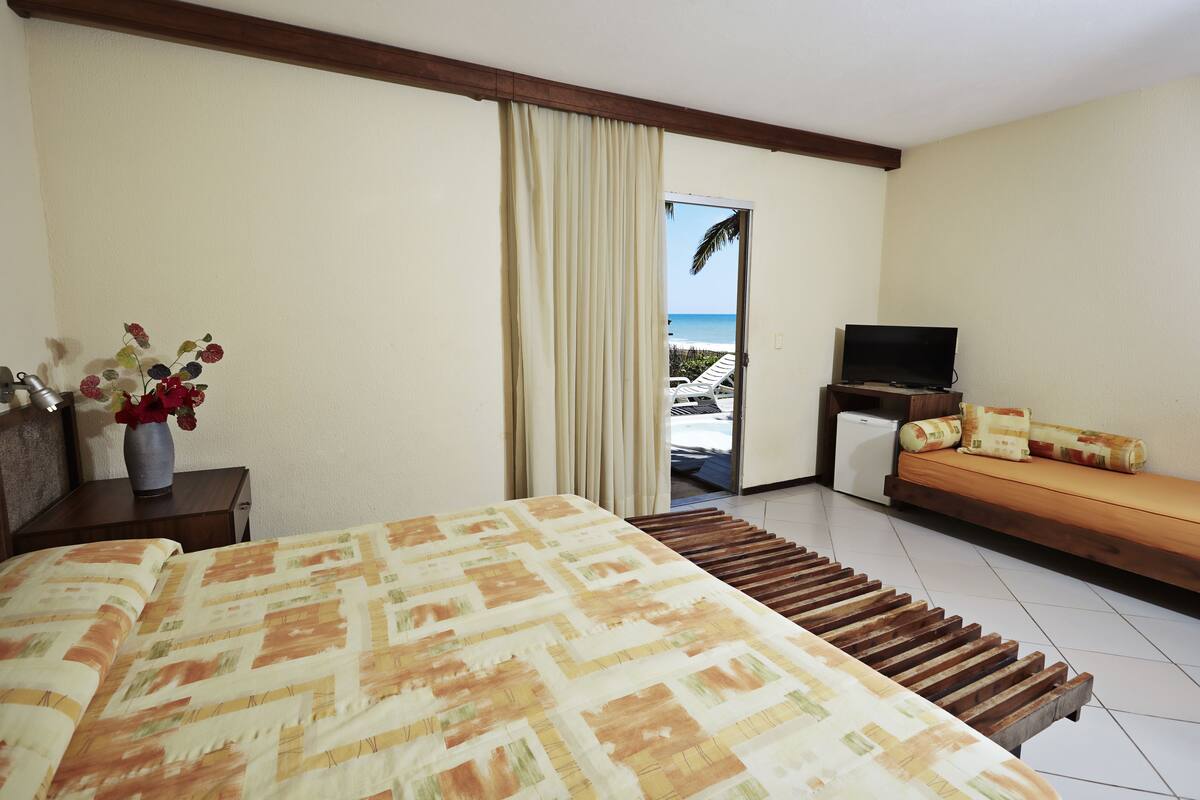 Habitación de hotel con cama, televisor, sofá y vista a la playa.