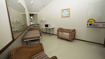 A room with a wicker chair, a small table, a baby changing station, a sink, and a mirror.
