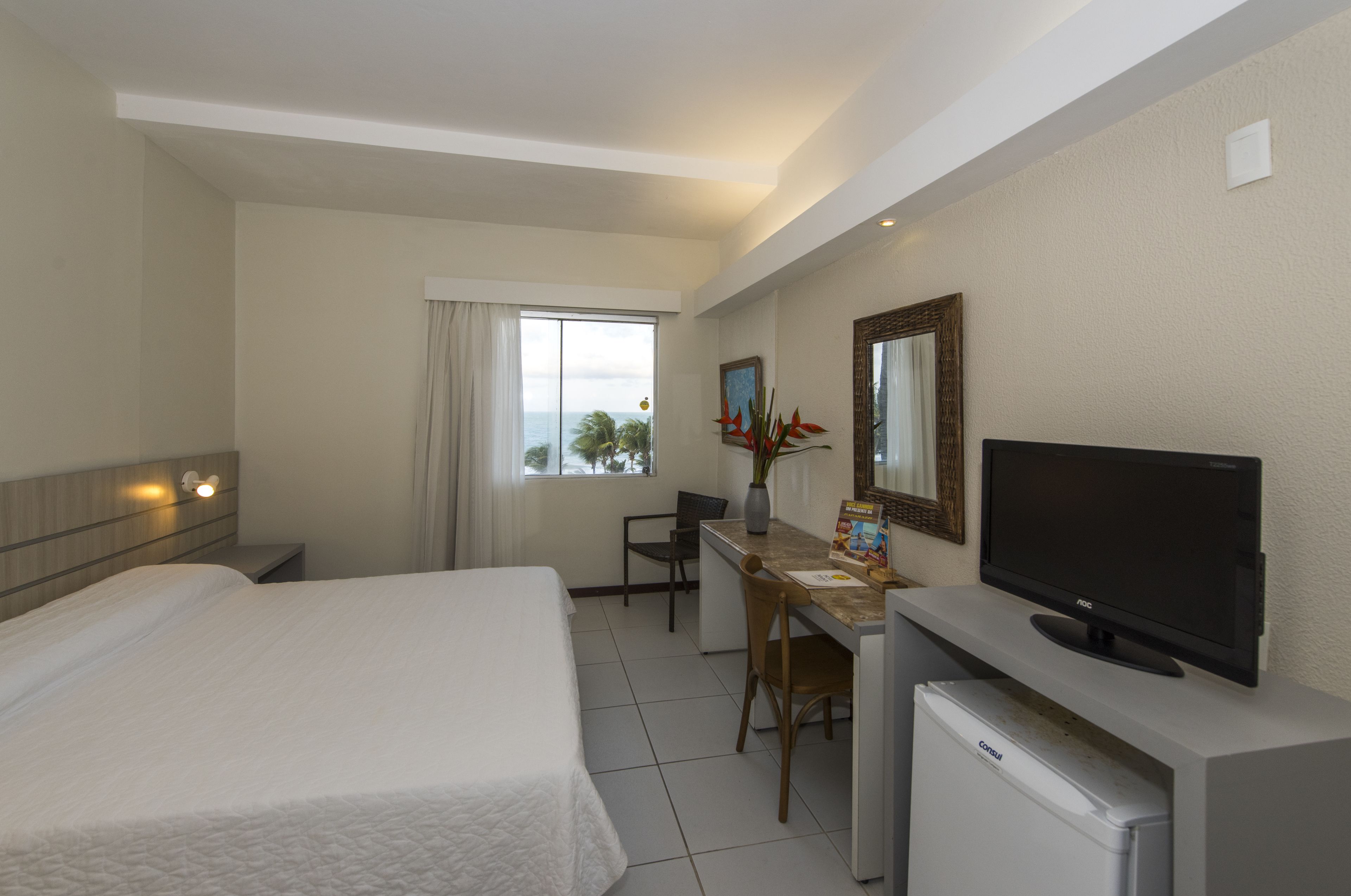 A hotel room with a bed, desk, television, and a small refrigerator.