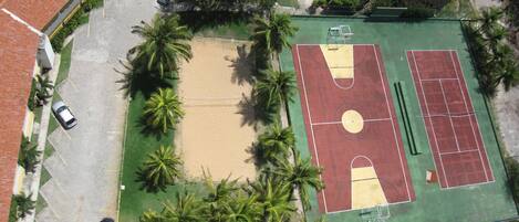 An aerial view of a sports court surrounded by palm trees and parked cars.