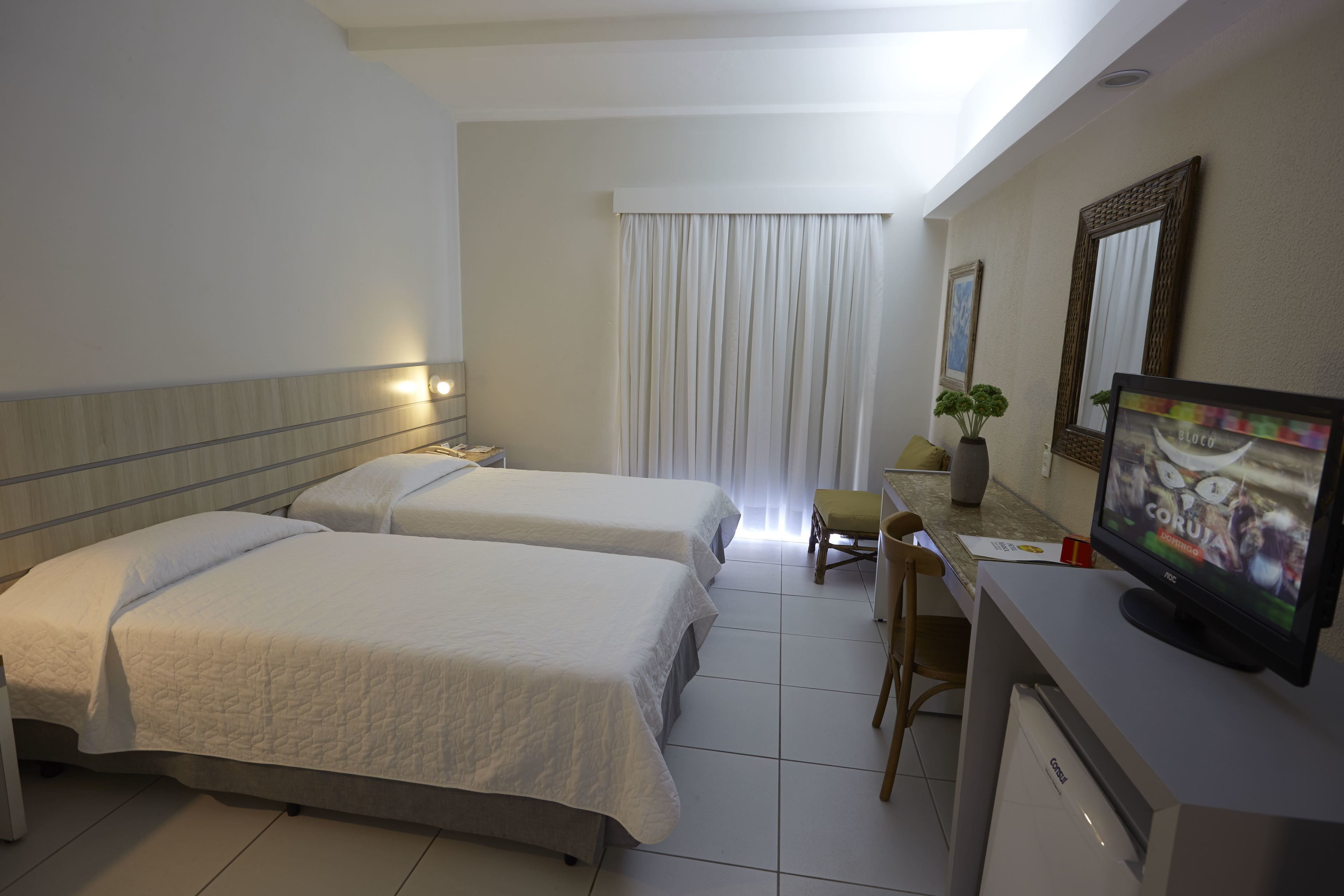 Une chambre d’hôtel avec deux lits, un bureau avec une télévision, une chaise et une fenêtre avec des rideaux.