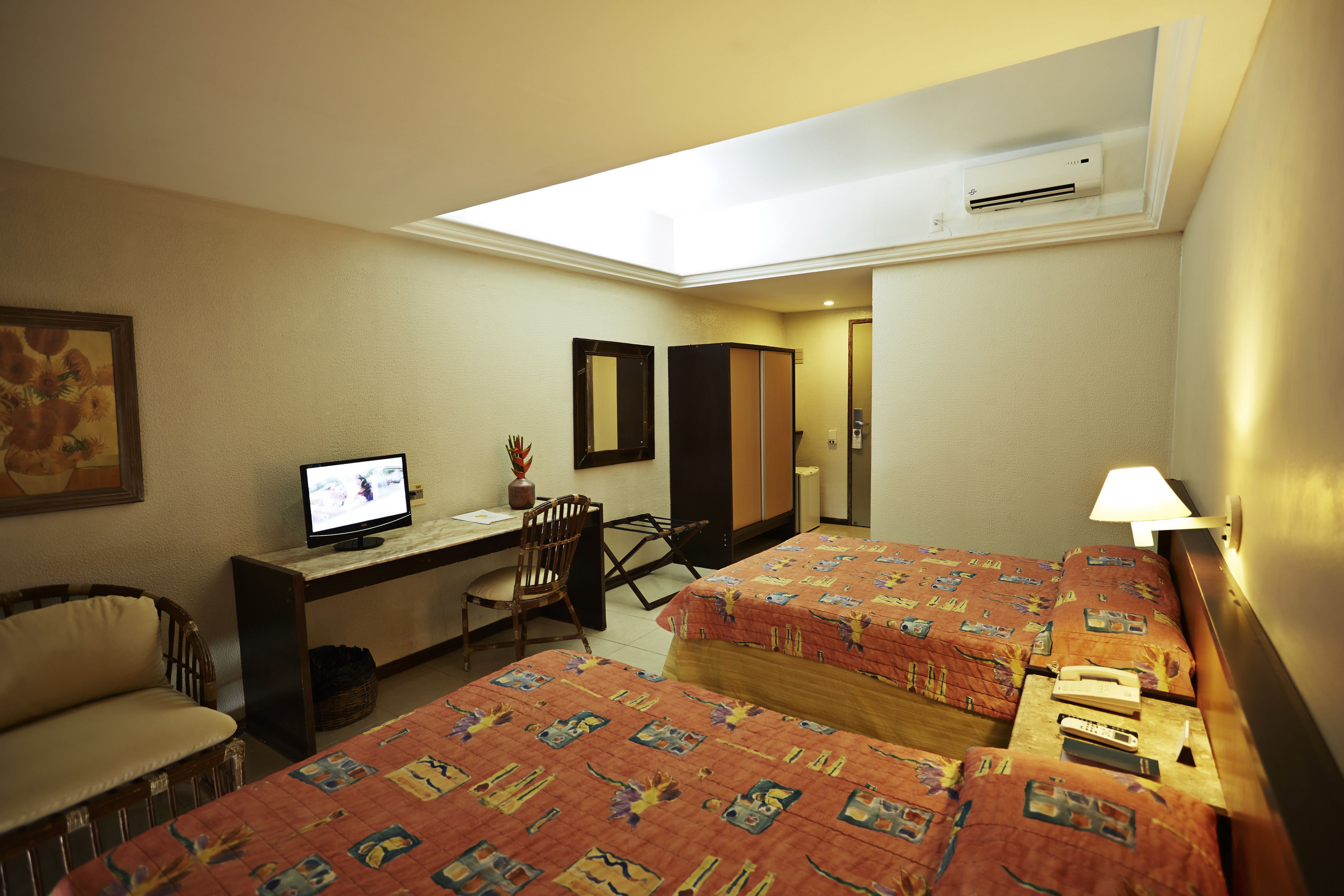 A hotel room with two beds, a desk, a chair, a TV, and a lamp.