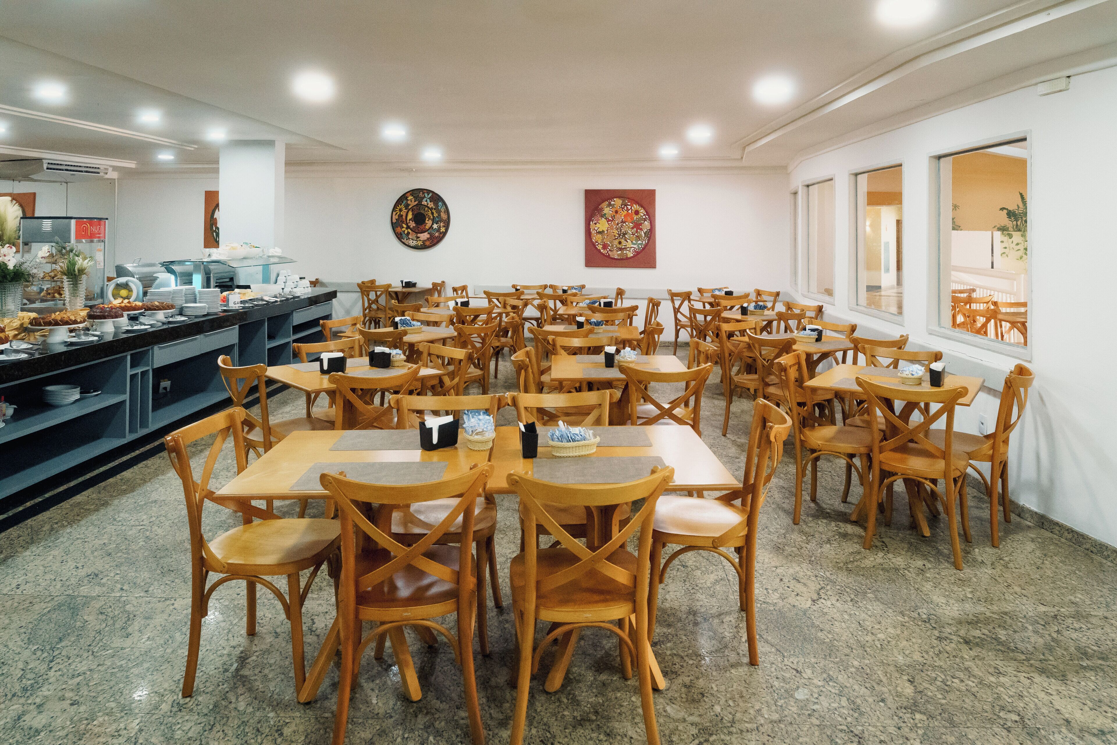 Un comedor con varias mesas y sillas, una barra de buffet y obras de arte en las paredes.