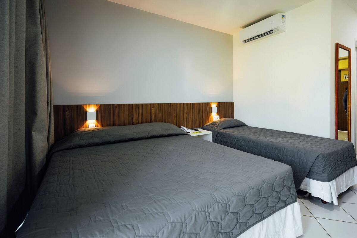 A hotel room with two beds, a wooden headboard, an air conditioning unit, and a nightstand with a lamp.