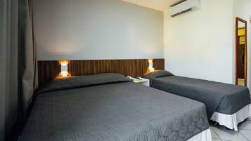 Een hotelkamer met twee bedden, een houten hoofdbord, een airconditioning en een nachtkastje met een lamp.