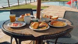 A round table with plates of food, a drink, and a view of a pool and beach. - EL ARAM NATAL MAR (Natal)