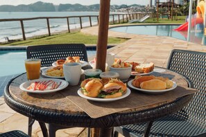 A round table with plates of food, a drink, and a view of a pool and beach. - EL ARAM NATAL MAR (Natal)