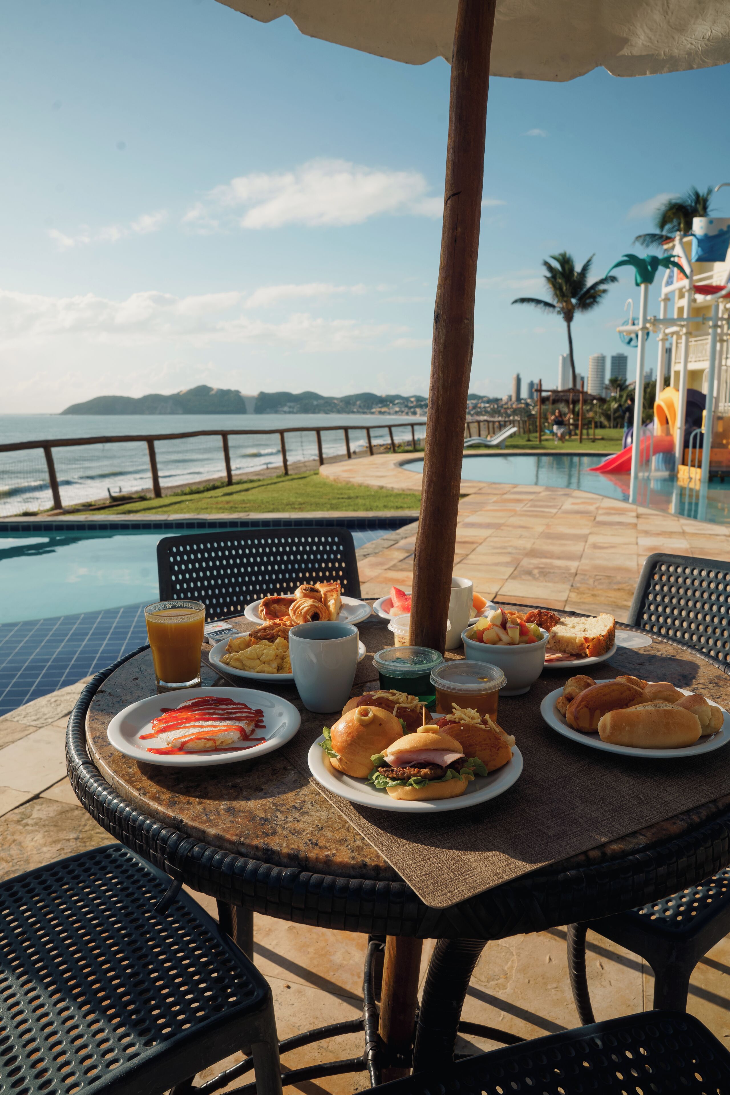 A dining table with food and drinks, a poolside view, and a wooden pole.