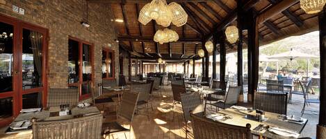 An indoor dining area with wicker furniture, brick walls, and hanging light fixtures.
