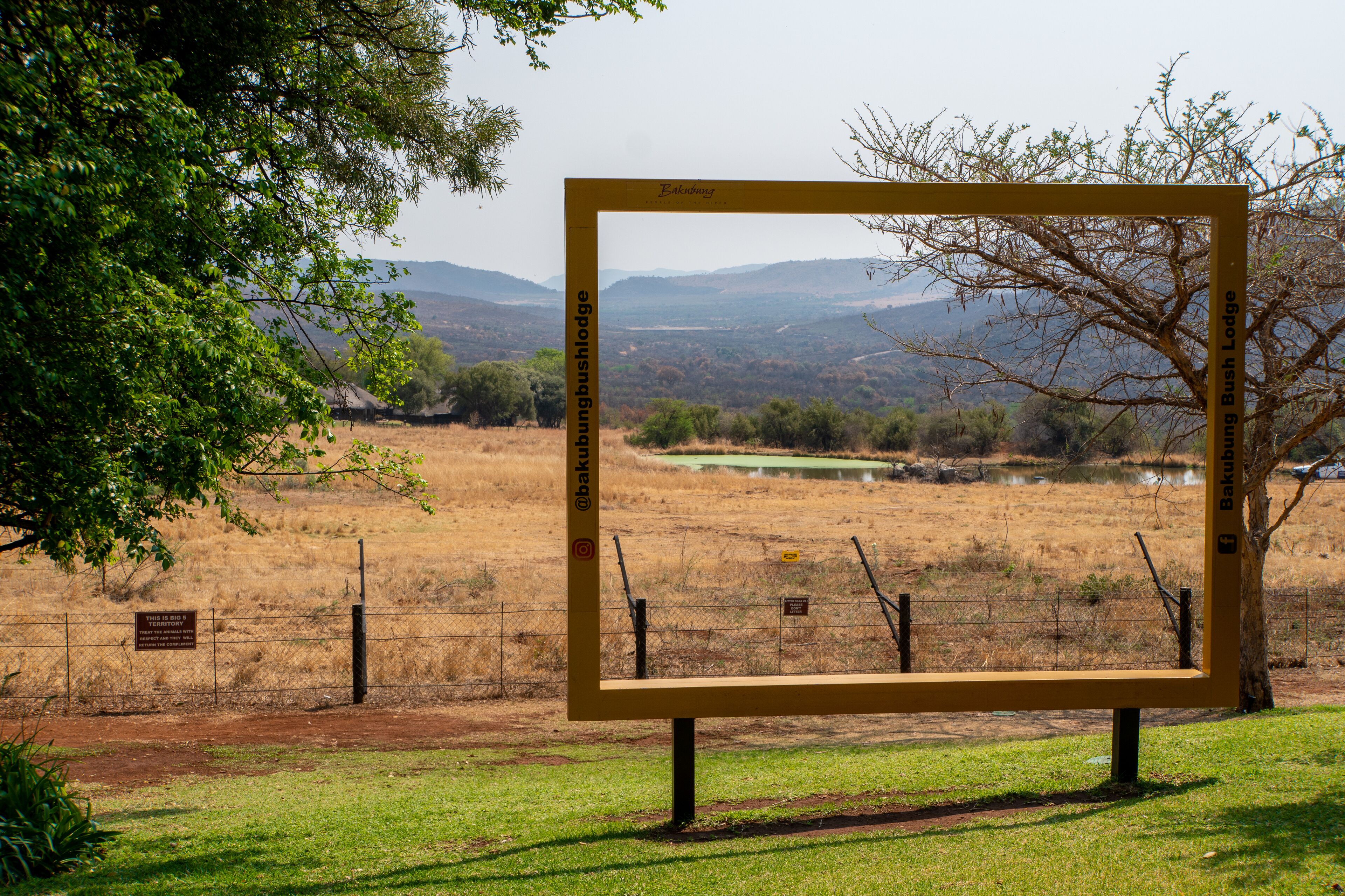 A framed view of a landscape with a sign reading "Bakubush Lodge."