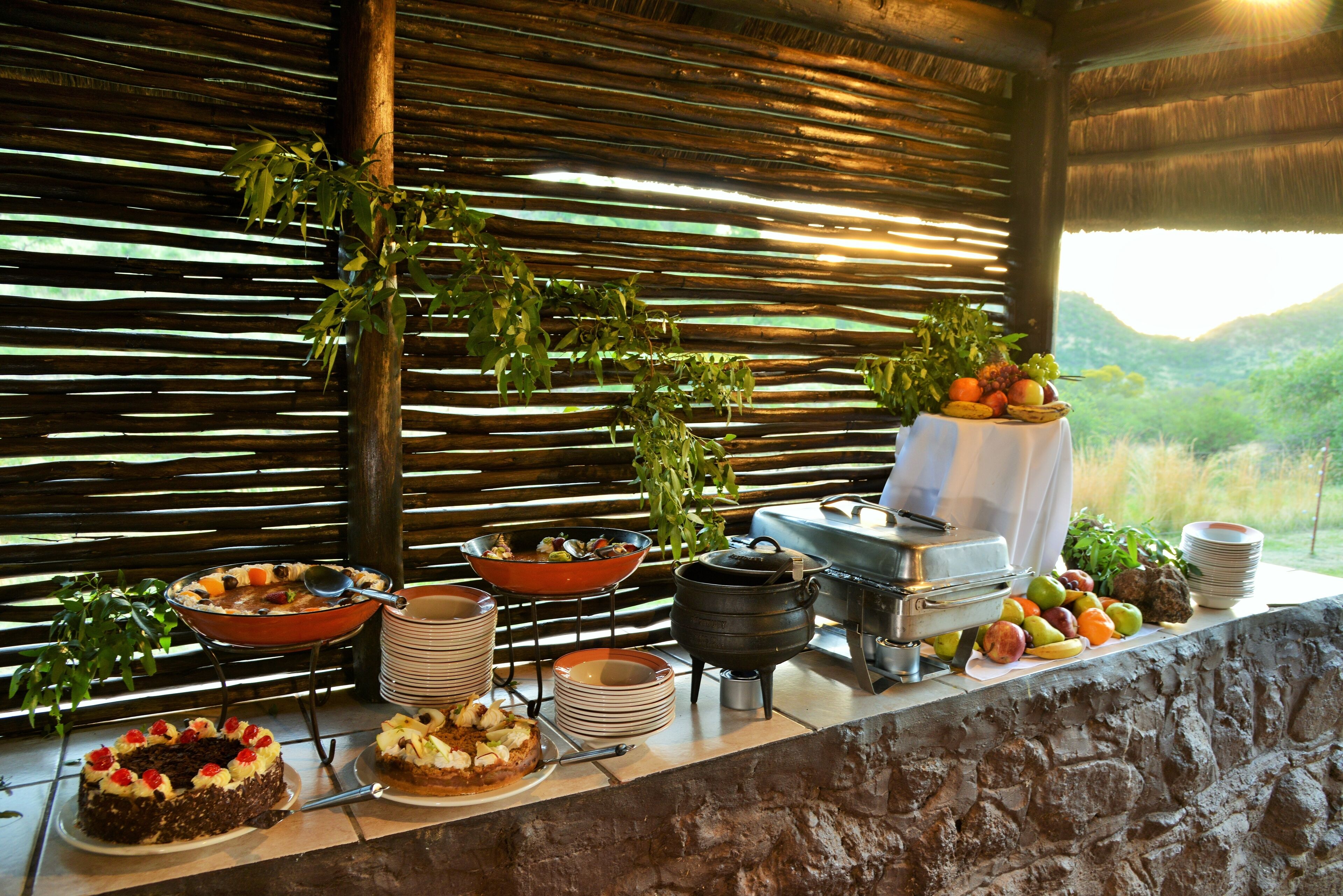 A buffet setup with various dishes, a fruit display, and a scenic outdoor view.