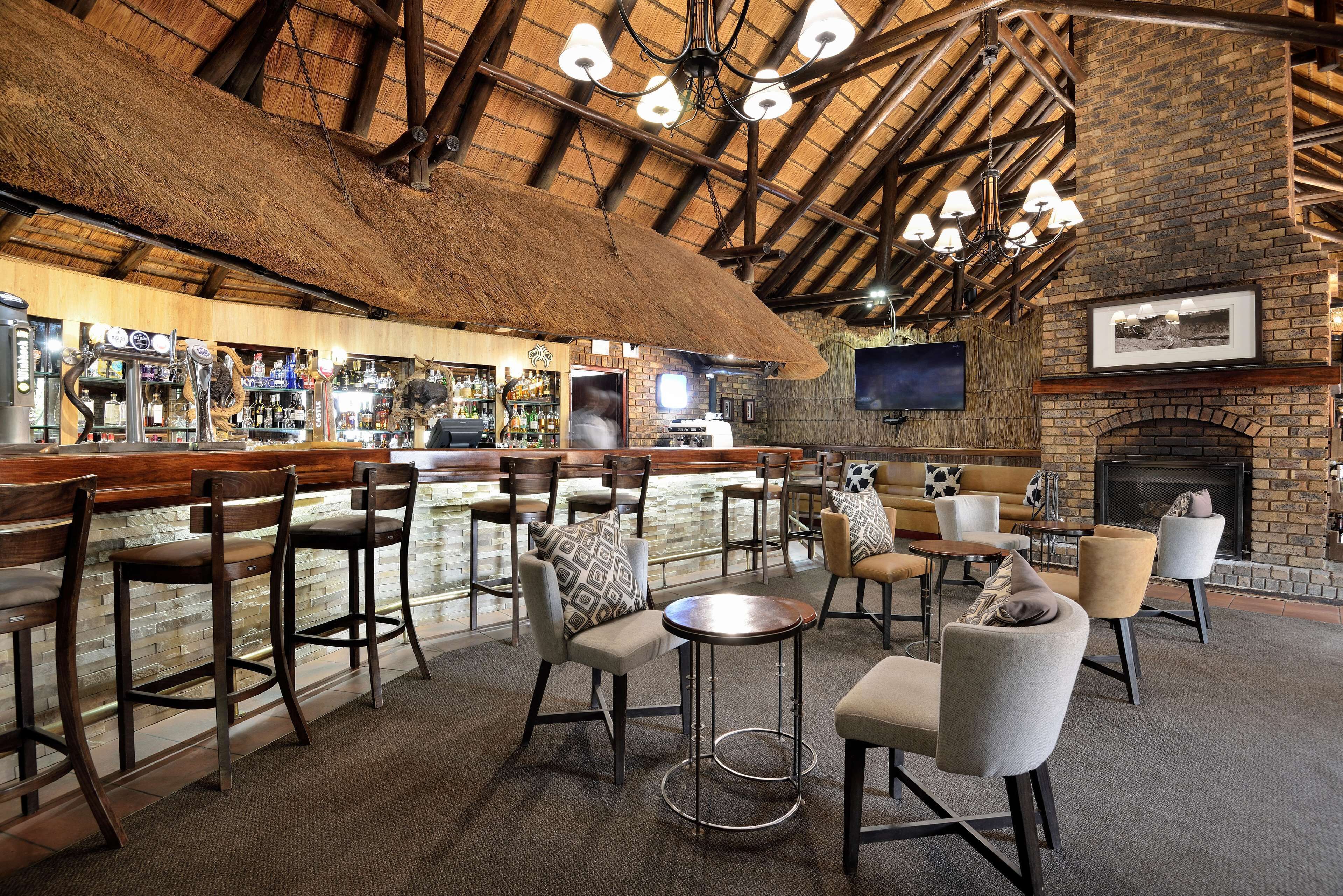 A bar area with stools and tables, a brick fireplace, and a television mounted on the wall.