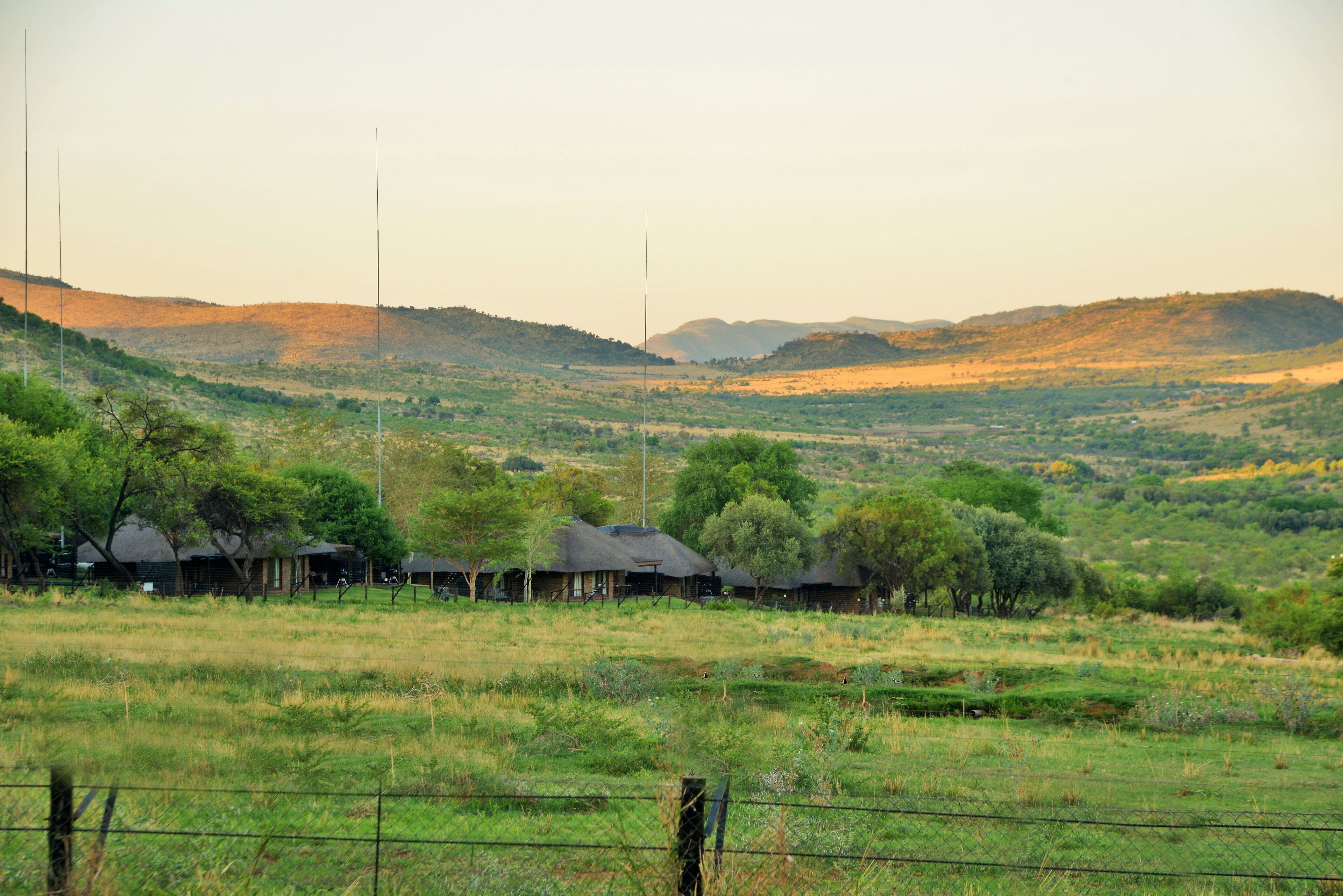 A rural landscape with thatched-roof huts and a fenced field.