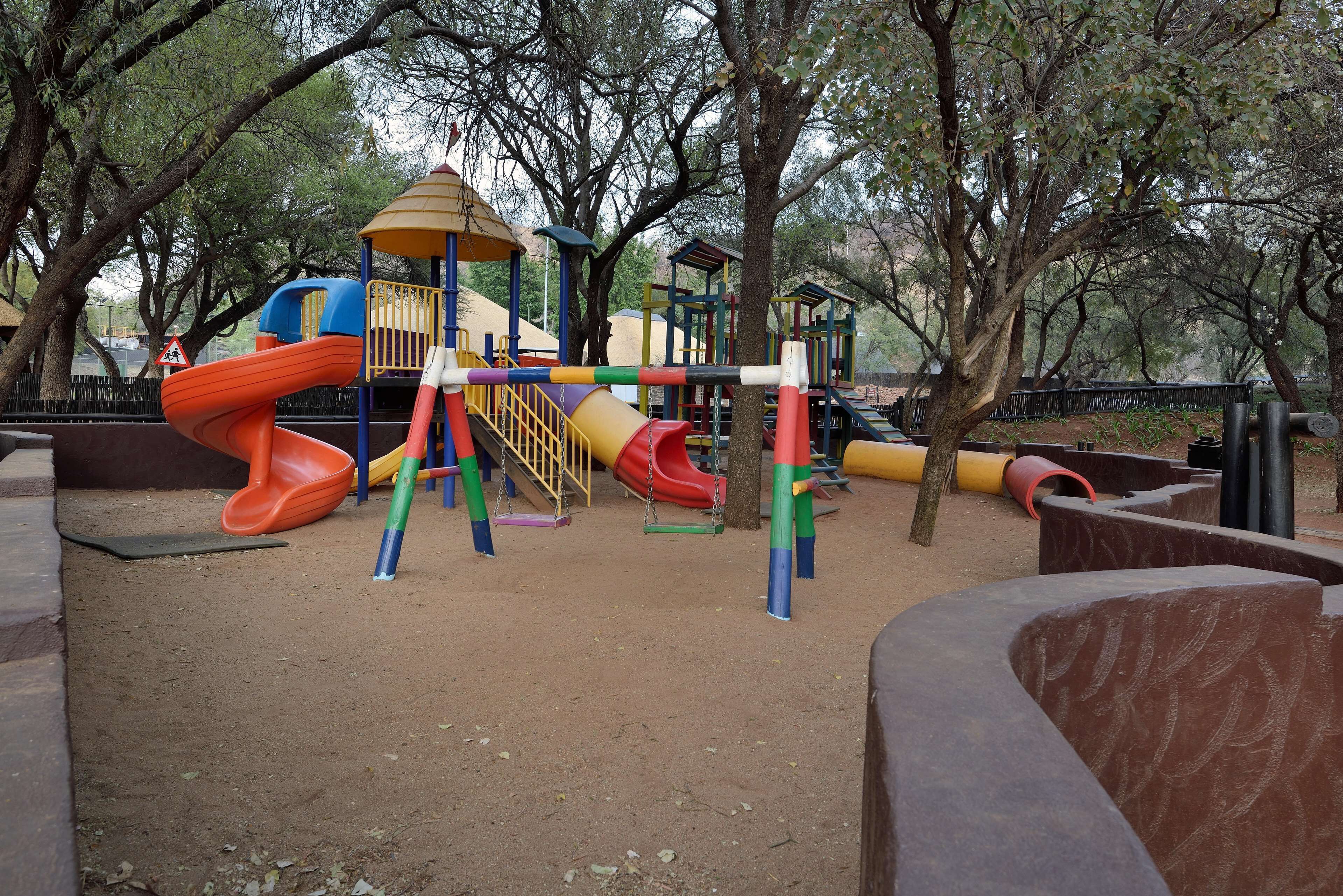 A playground with slides and climbing structures surrounded by trees.